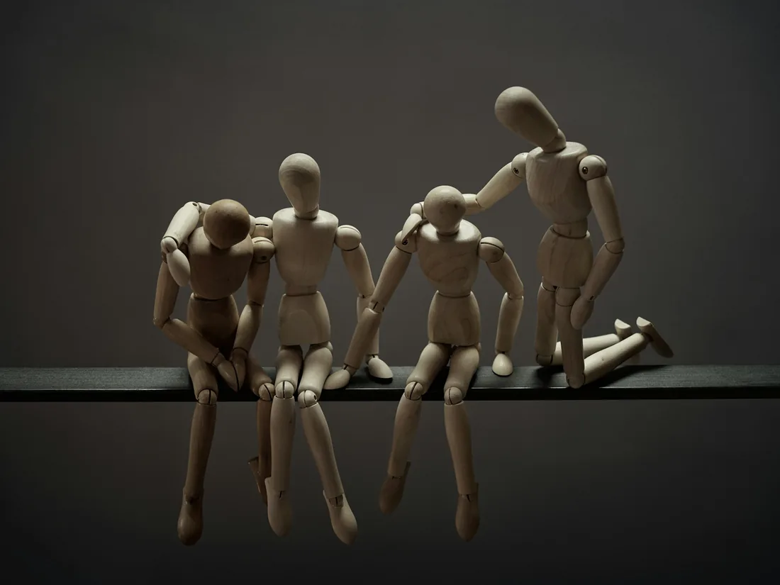Figuras articuladas de madera colocadas en el borde de una mesa de taller, iluminadas de forma tenue